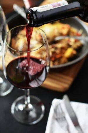 Close-up of red wine being poured into a glass at a romantic dinner setting with food in the background.